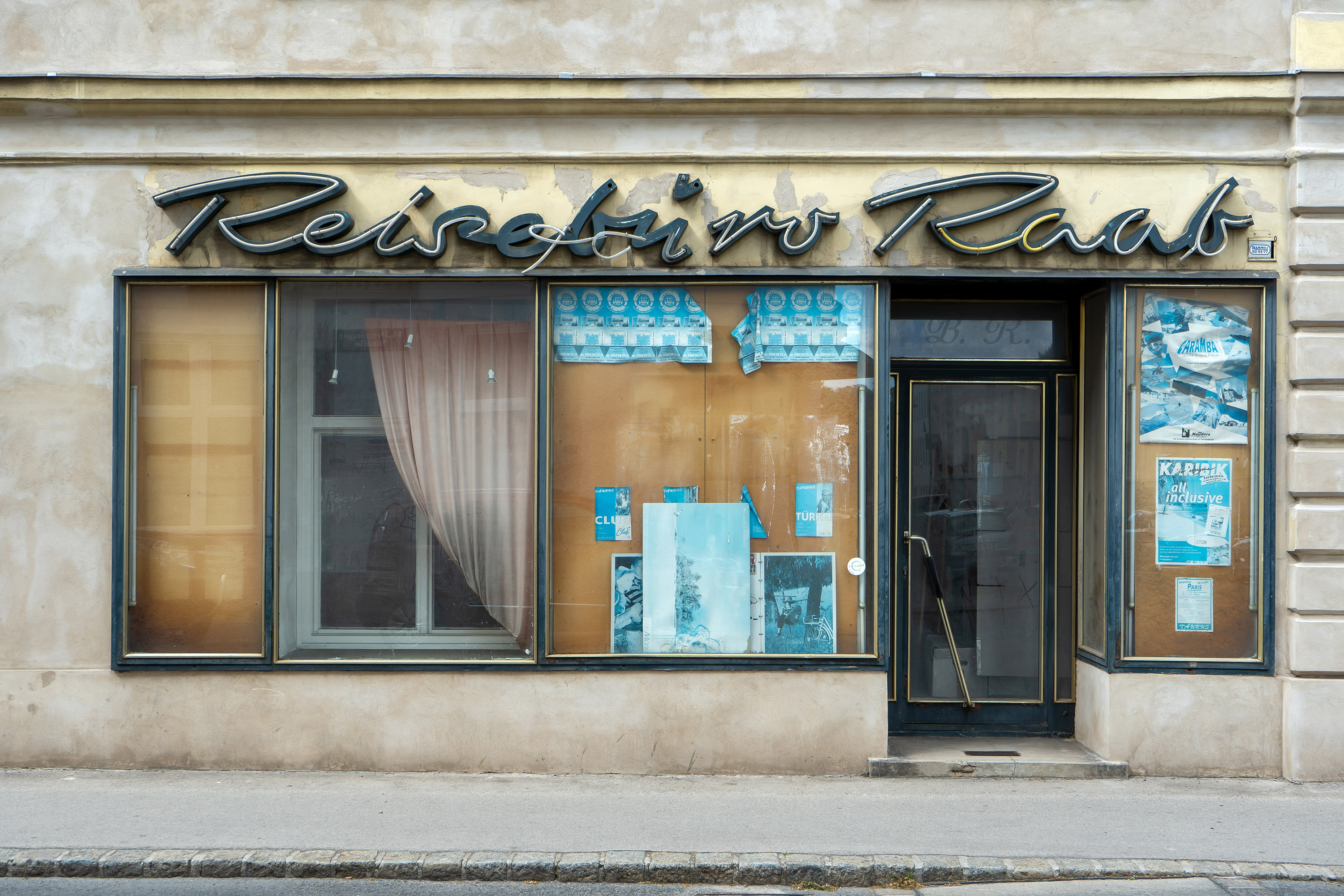 Foto: Georg Scherer/wienschauen.at Foto eines leerstehenden Reisebüros, Firmenname "Reisebüro Raab" ist schon teilweise runtergefallen, Schaufenster sind großteils leer, ein paar ausgebleichte alte Plakate von Reiseveranstaltungen hängen noch.